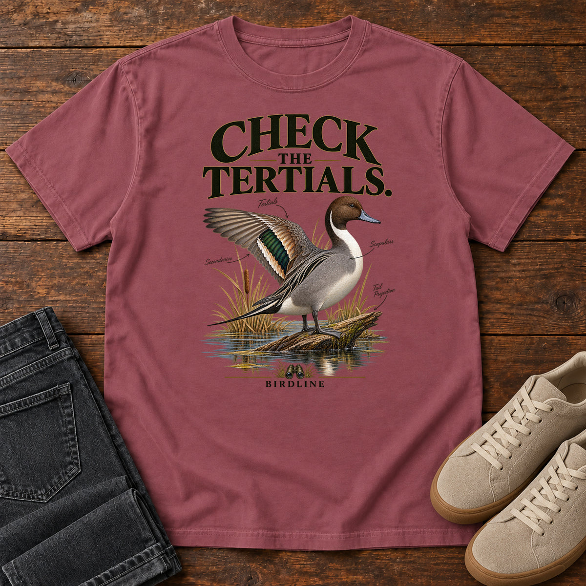 Brick Check the Tertials Duck T-Shirt with a duck raising one wing beside reeds and water; front flat lay on wood.