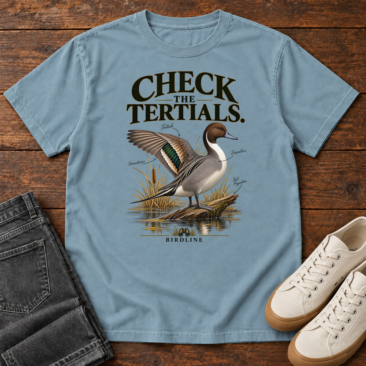 Ice Blue Check the Tertials Duck T-Shirt with a duck raising one wing beside reeds and water; front flat lay on wood.