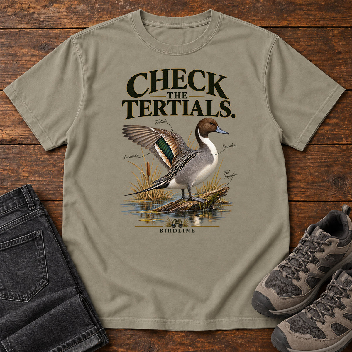 Sandstone Check the Tertials Duck T-Shirt with a duck raising one wing beside reeds and water; front flat lay on wood.