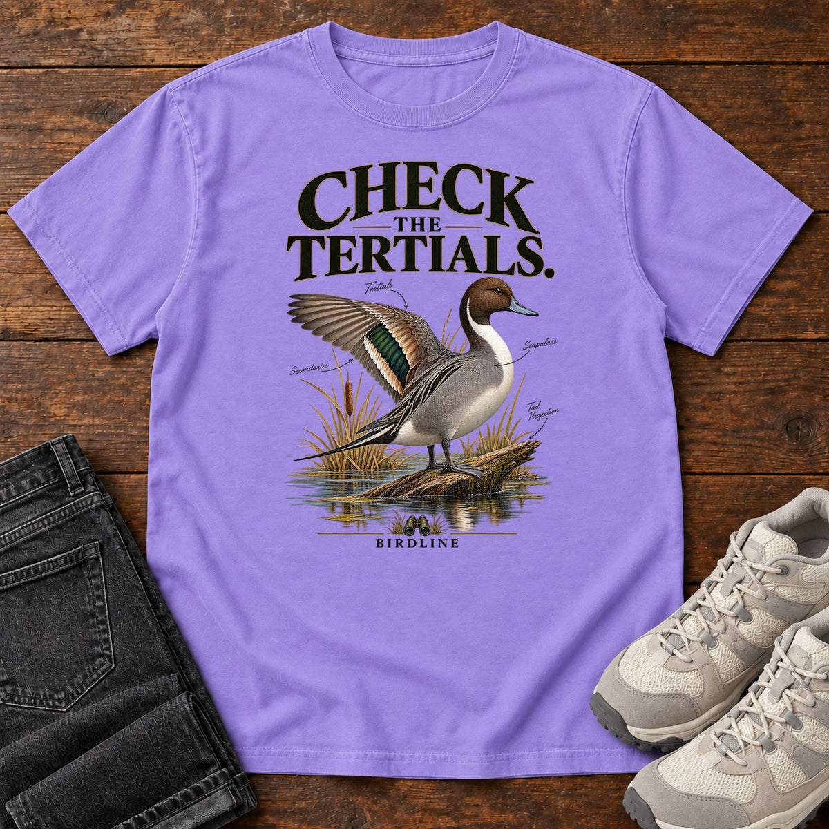 Violet Check the Tertials Duck T-Shirt with a duck raising one wing beside reeds and water; front flat lay on wood.