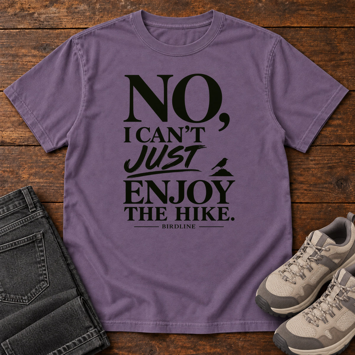 Grape No I Can't Just Enjoy the Hike T-Shirt with bold black lettering and a small bird silhouette, front flat lay on wood.