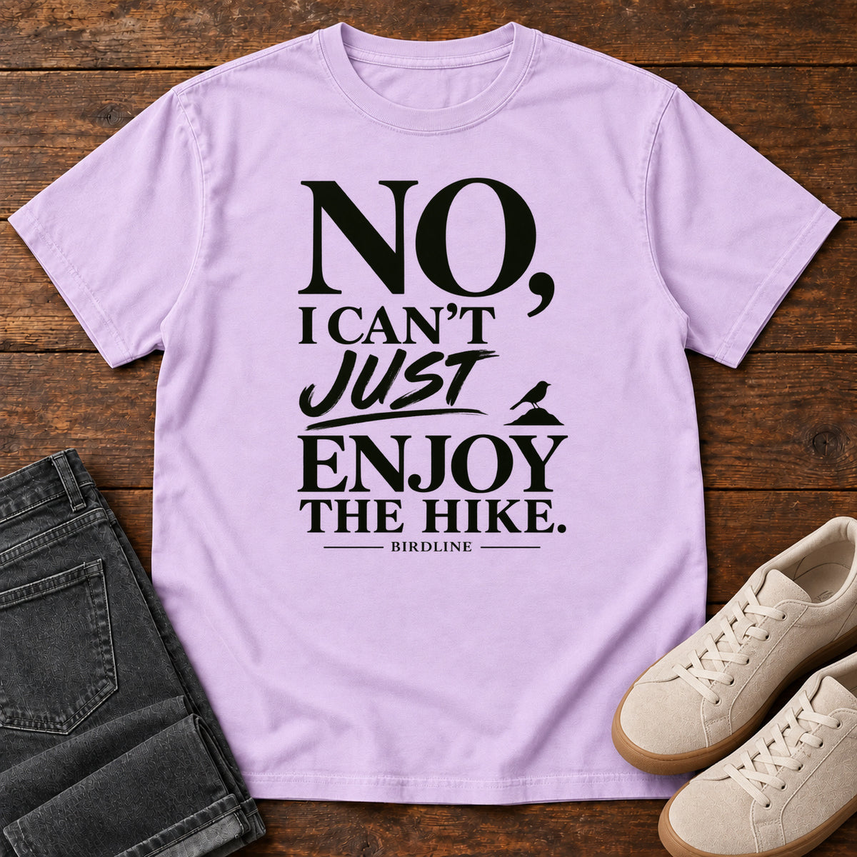Orchid No I Can't Just Enjoy the Hike T-Shirt with bold black lettering and a small bird silhouette, front flat lay on wood.