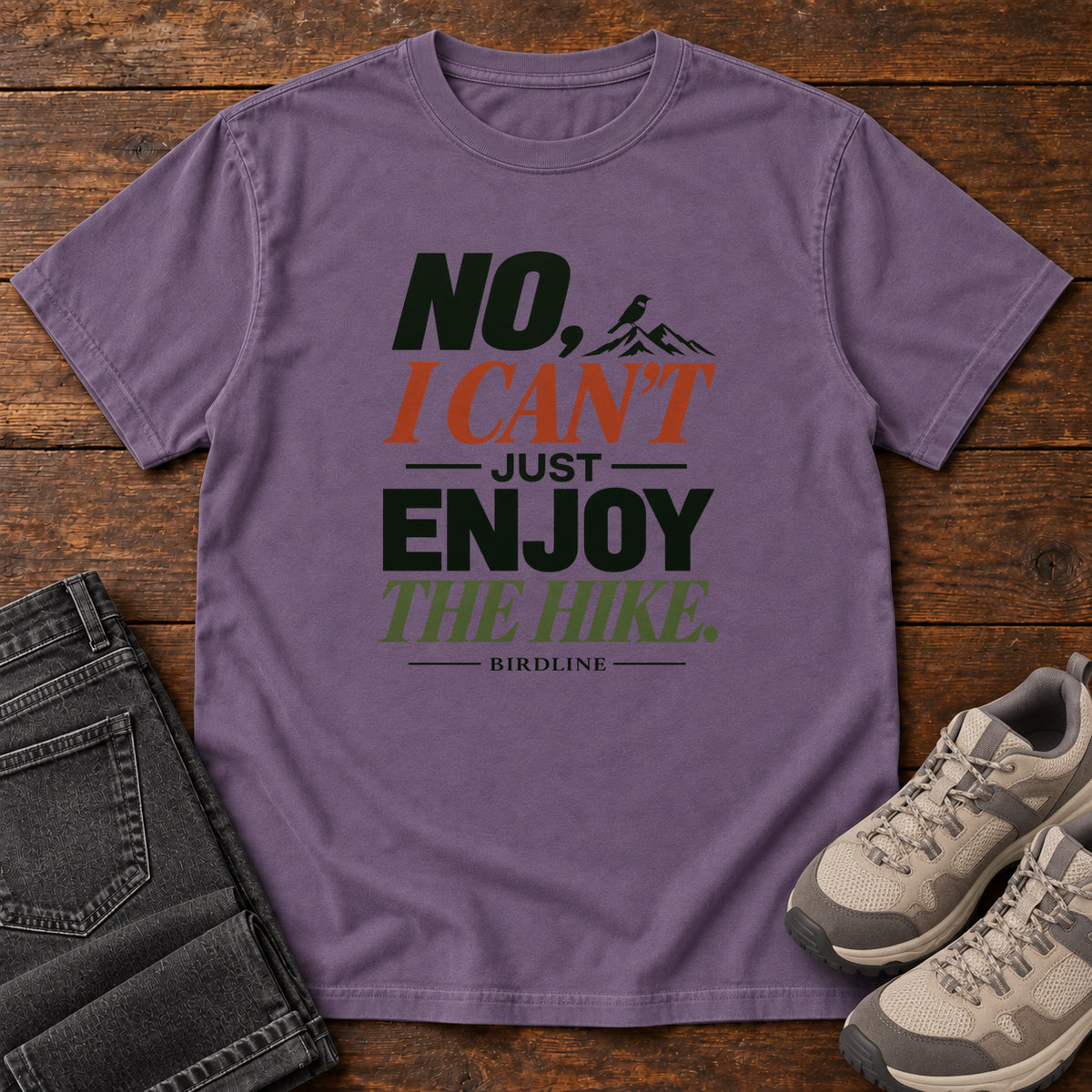 No I Can't Just Enjoy the Hike T-Shirt – Color Block in Grape, front laid flat on wood, featuring stacked green and rust slogan lettering and a small mountain graphic.
