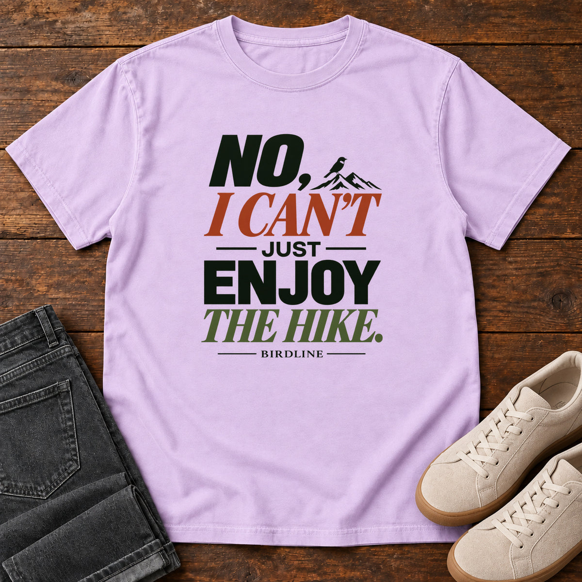 No I Can't Just Enjoy the Hike T-Shirt – Color Block in Orchid, front laid flat on wood, featuring stacked green and rust slogan lettering and a small mountain graphic.