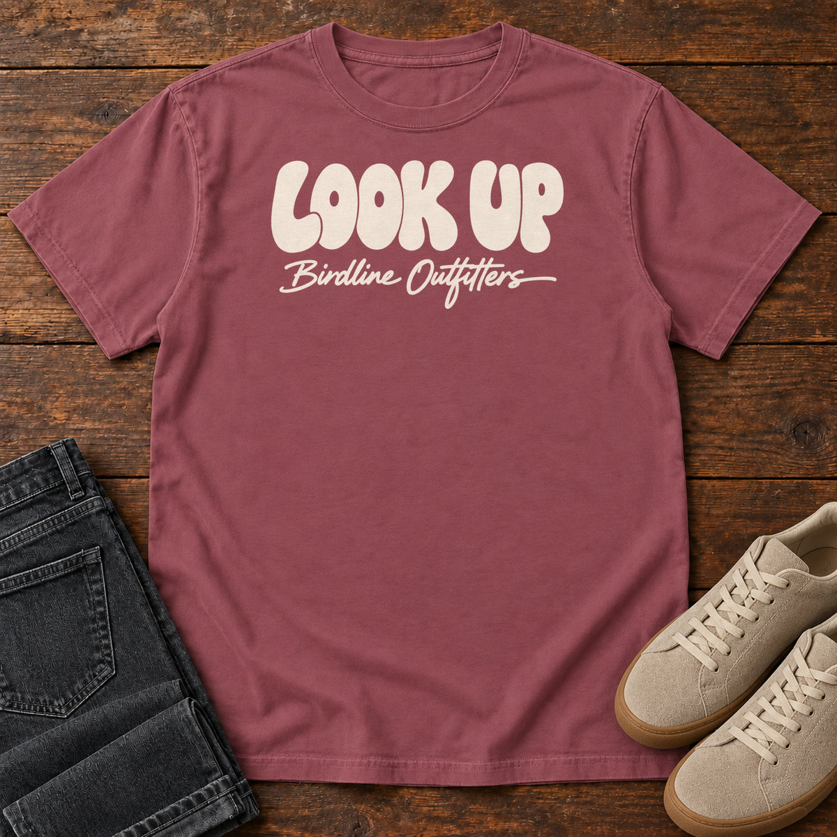 Look Up T-shirt in Brick, front laid flat on wood, featuring large rounded cream LOOK UP lettering above Birdline Outfitters script.