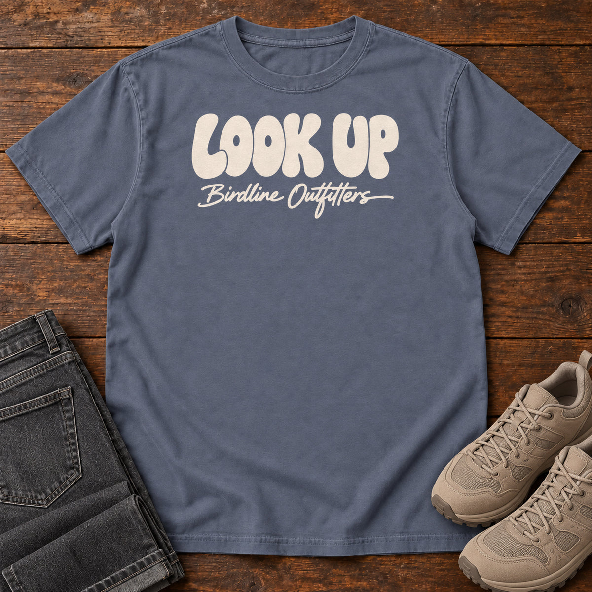 Look Up T-shirt in Denim, front laid flat on wood, featuring large rounded cream LOOK UP lettering above Birdline Outfitters script.