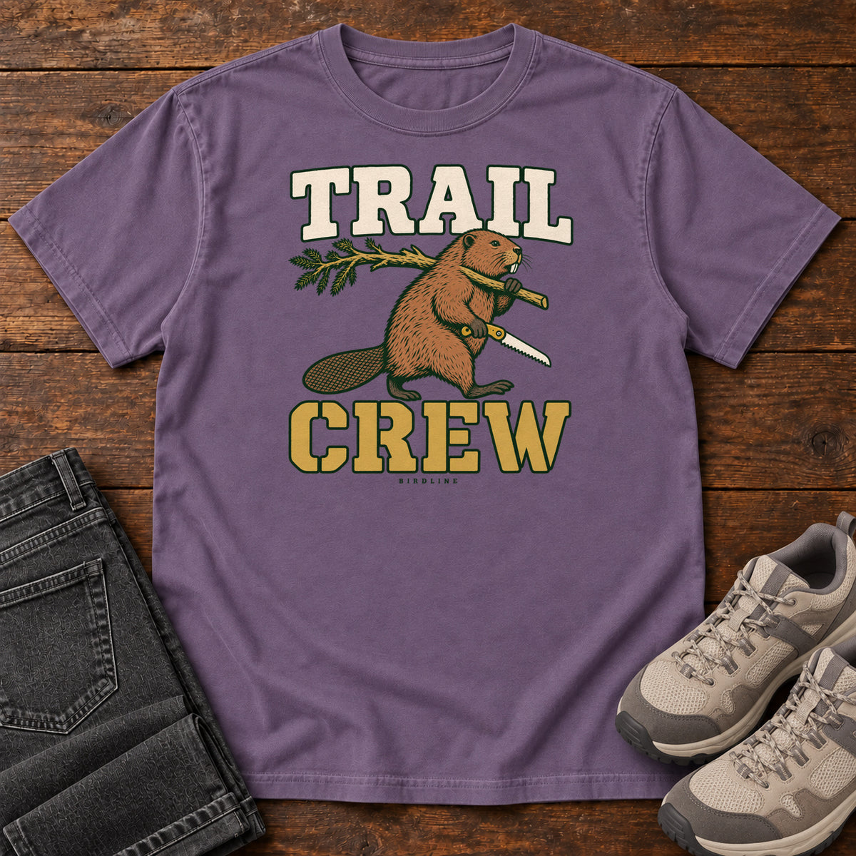 Grape Trail Crew Foreman T-Shirt with a beaver carrying a leafy branch and saw beneath Trail Crew lettering; front flat lay on wood.