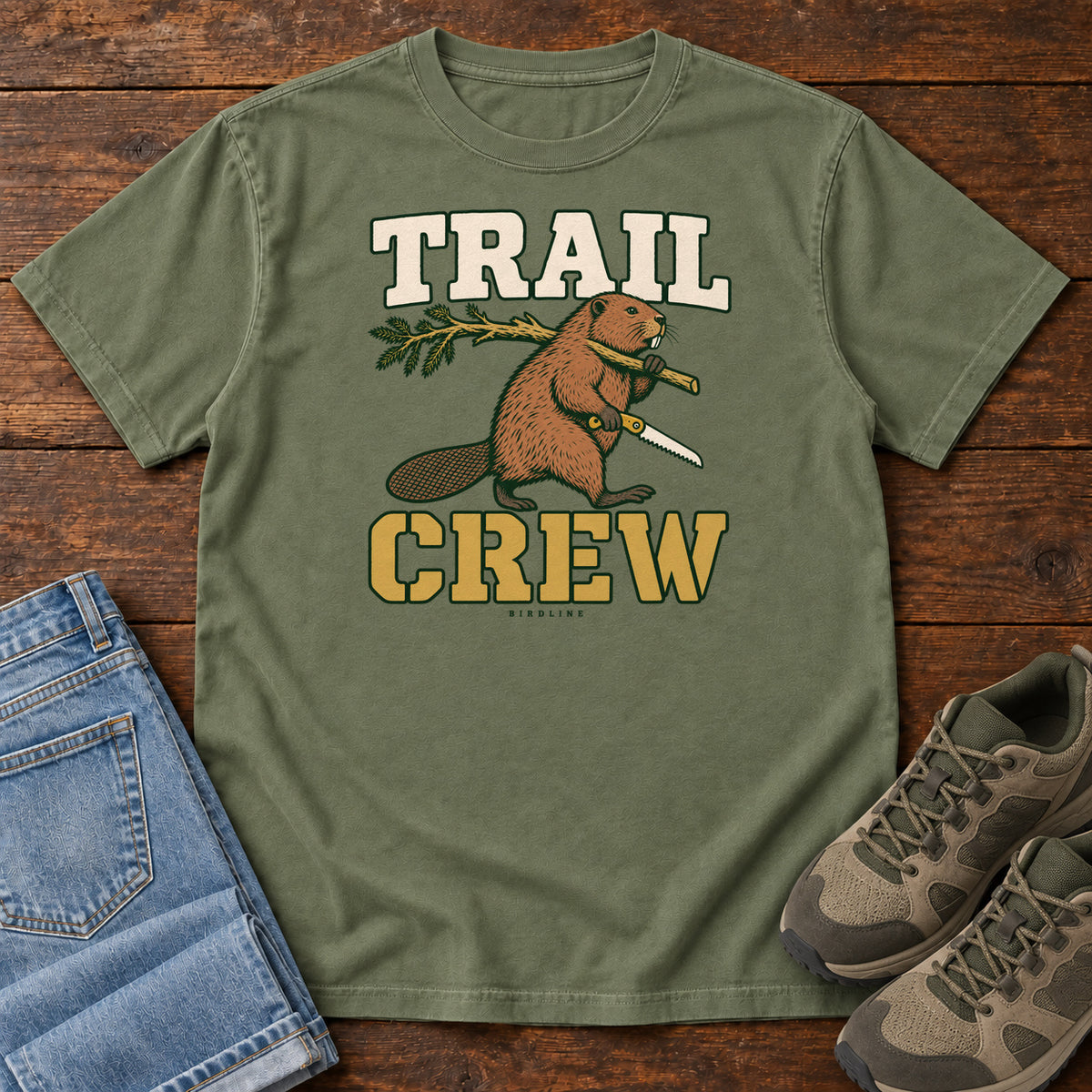 Moss Trail Crew Foreman T-Shirt with a beaver carrying a leafy branch and saw beneath Trail Crew lettering; front flat lay on wood.