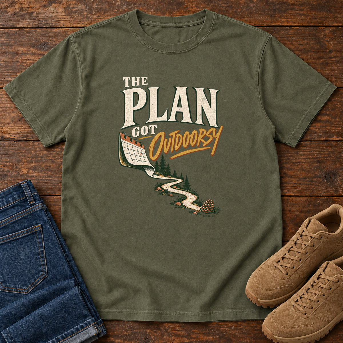 Sage The Plan Got Outdoorsy T-Shirt with cream-and-gold lettering above a calendar turning into a winding trail, front flat lay on wood.