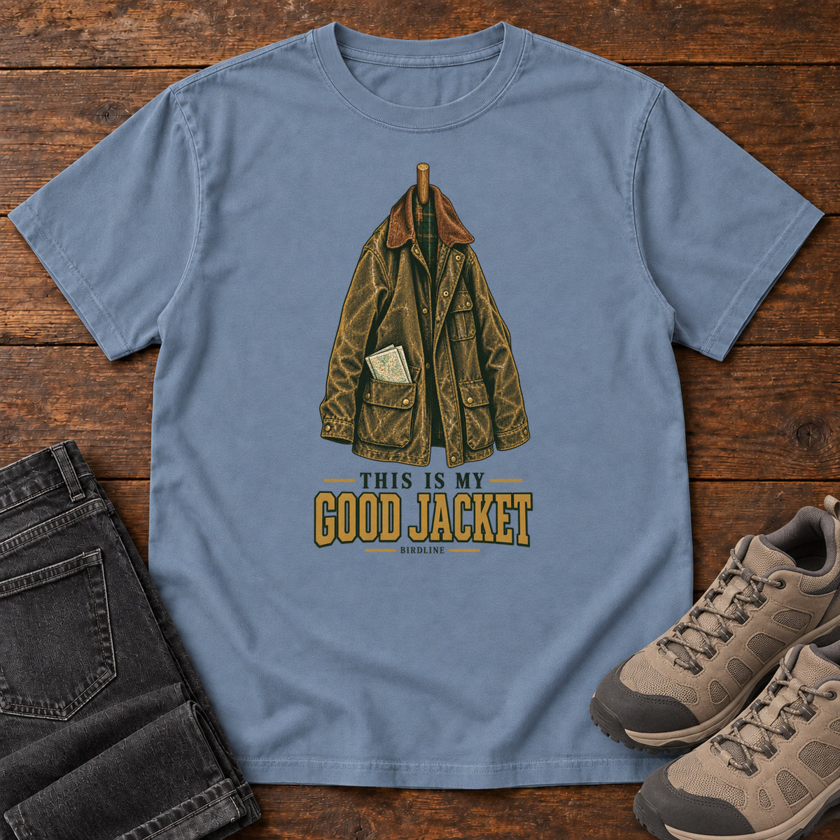 Blue Jean This Is My Good Jacket T-Shirt with a hanging outdoor jacket and This Is My Good Jacket lettering; front flat lay on wood.