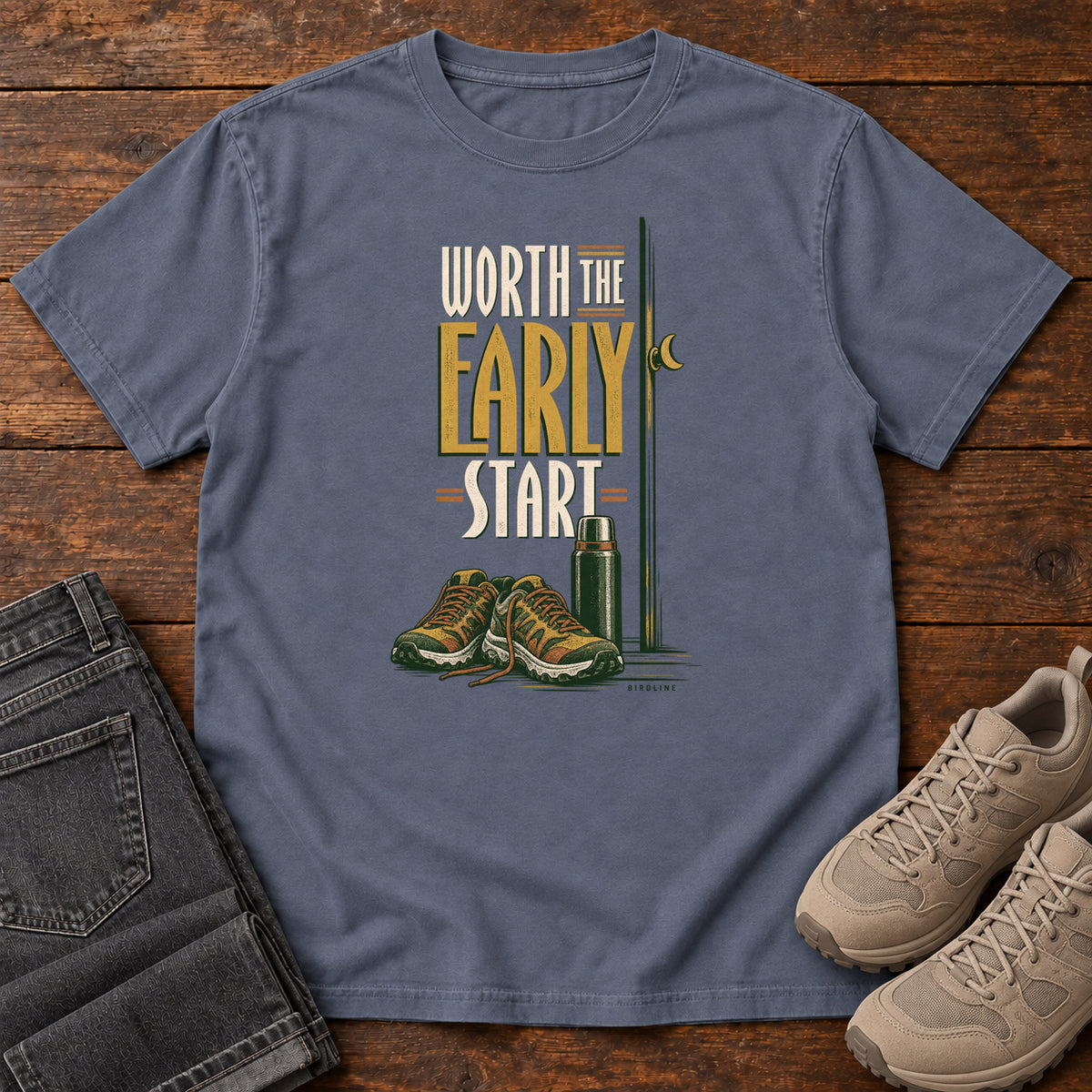 Denim Worth the Early Start T-Shirt with hiking shoes, a thermos, a walking pole and a crescent moon; front flat lay on wood.
