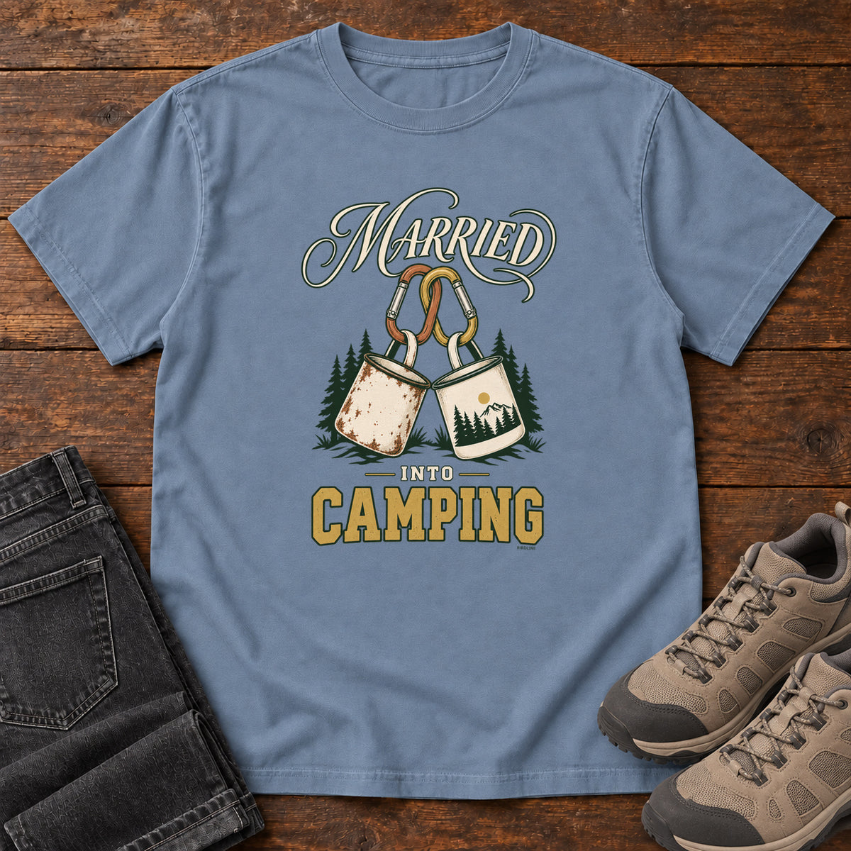 Blue Jean Married into Camping T-Shirt with two camp mugs hanging from carabiners between cream and gold lettering, front flat lay on wood.