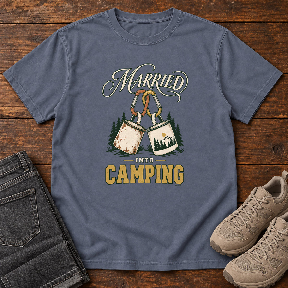Denim Married into Camping T-Shirt with two camp mugs hanging from carabiners between cream and gold lettering, front flat lay on wood.