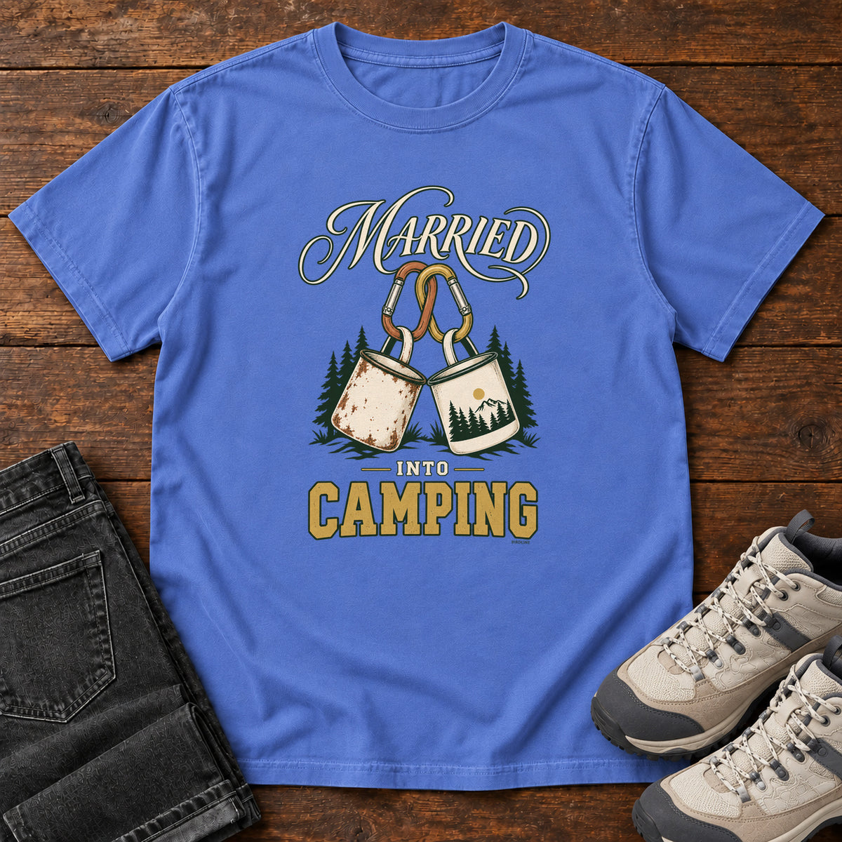 Mystic Blue Married into Camping T-Shirt with two camp mugs hanging from carabiners between cream and gold lettering, front flat lay on wood.
