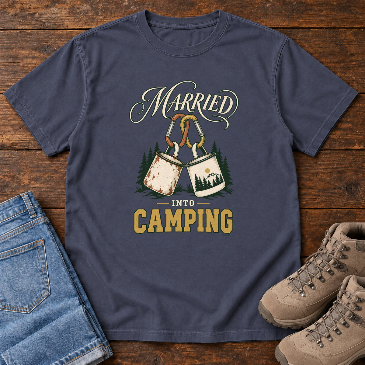 Navy Married into Camping T-Shirt with two camp mugs hanging from carabiners between cream and gold lettering, front flat lay on wood.