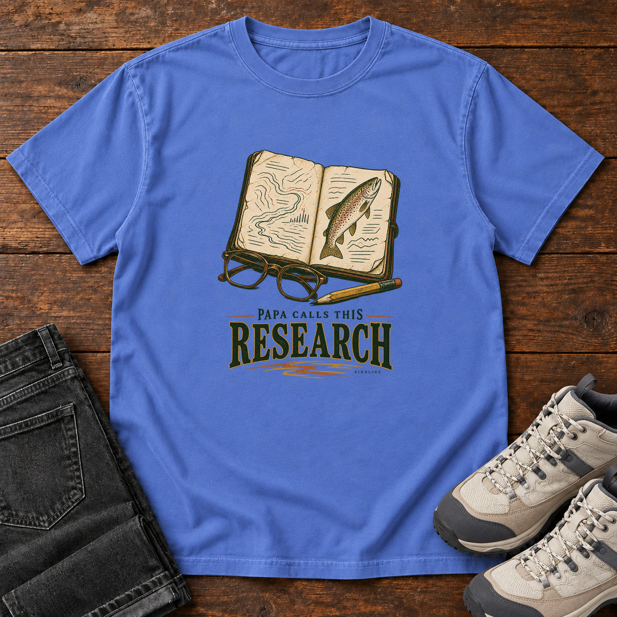 Mystic Blue Papa Calls This Research T-Shirt with an open field notebook showing a map and fish, with glasses and a pencil, front flat lay on wood.