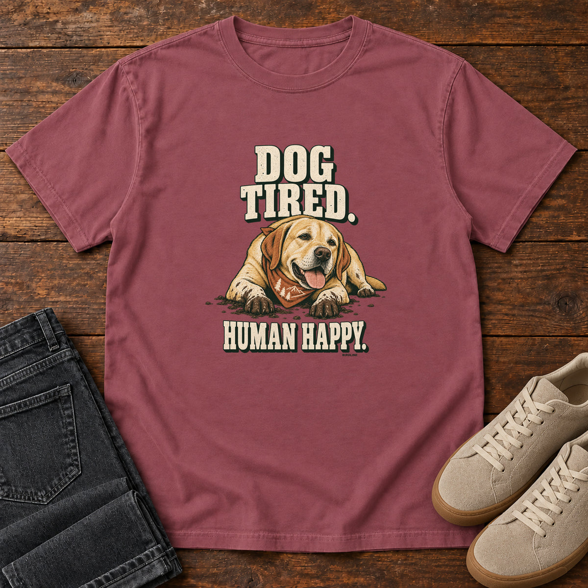 Dog Tired Human Happy T-Shirt in Brick, front laid flat on wood, featuring a resting golden-brown dog wearing an orange bandana between cream slogan lettering.