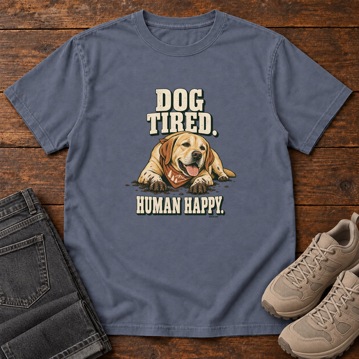 Dog Tired Human Happy T-Shirt in Denim, front laid flat on wood, featuring a resting golden-brown dog wearing an orange bandana between cream slogan lettering.