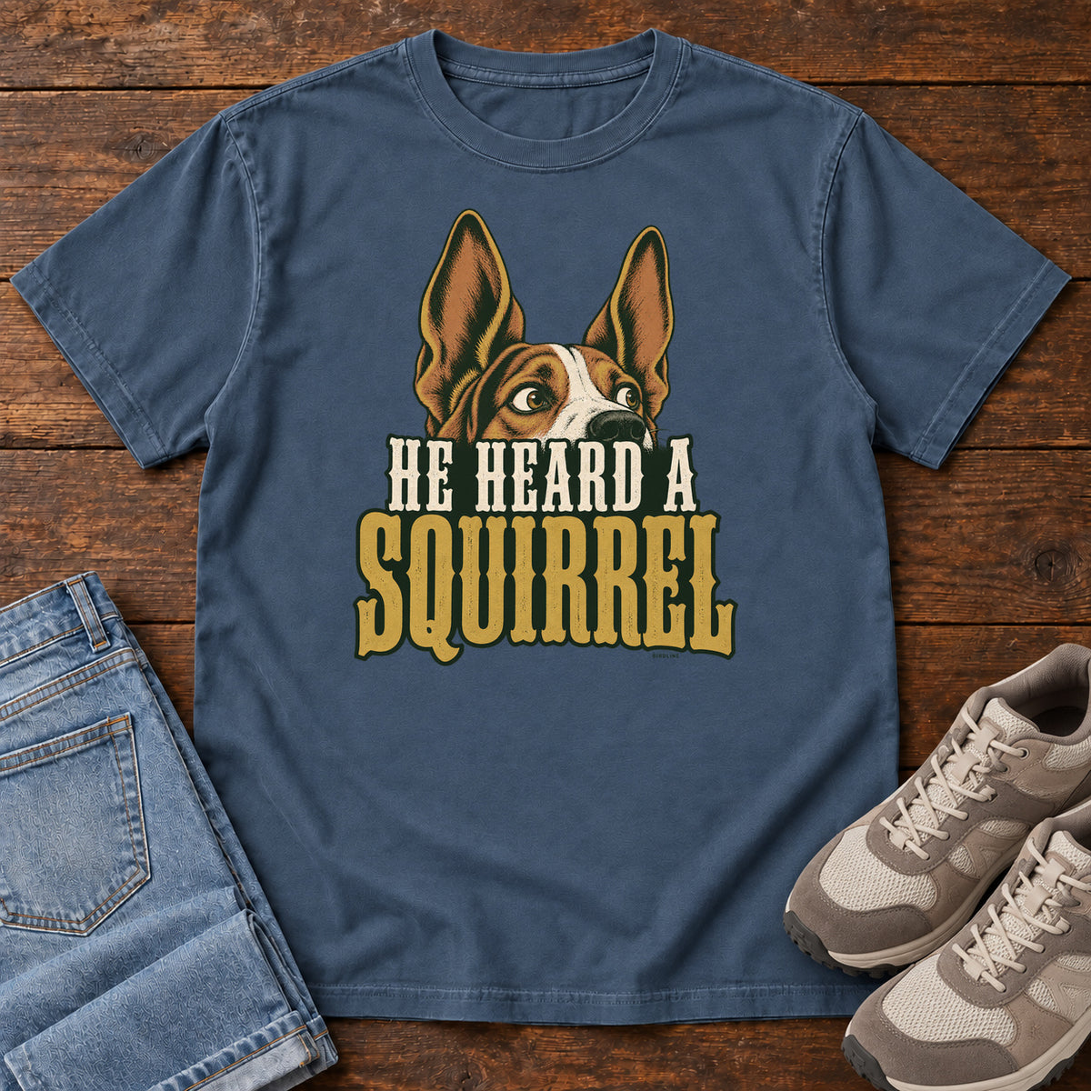 Midnight He Heard a Squirrel T-Shirt with an alert dog with upright ears above He Heard a Squirrel lettering; front flat lay on wood.