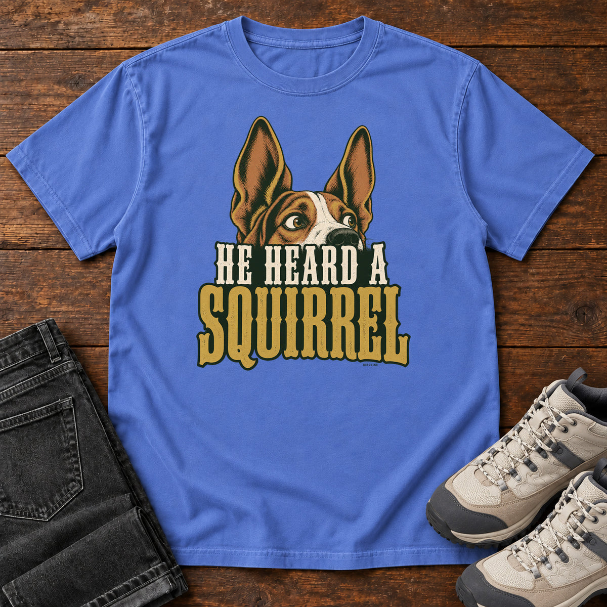 Mystic Blue He Heard a Squirrel T-Shirt with an alert dog with upright ears above He Heard a Squirrel lettering; front flat lay on wood.