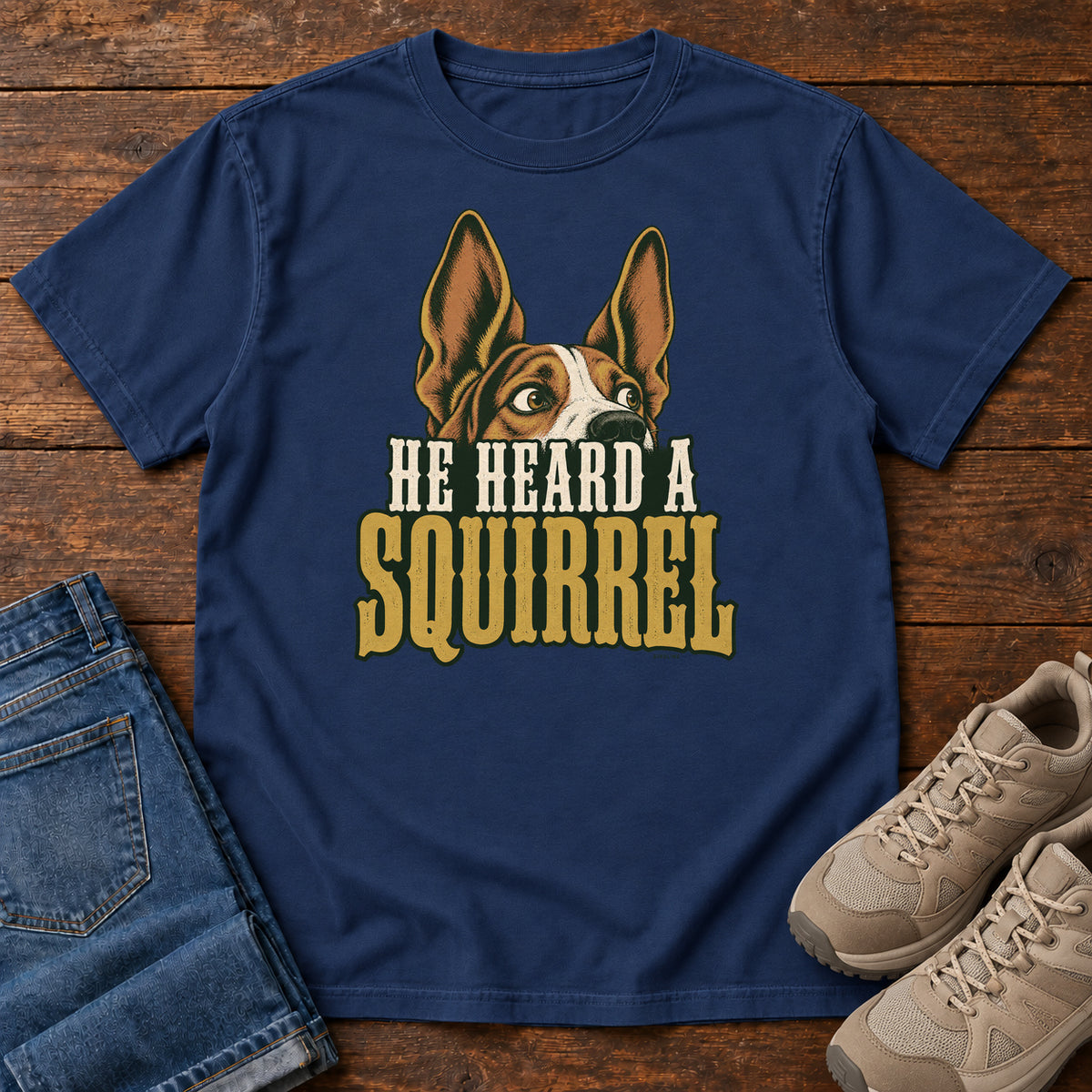 True Navy He Heard a Squirrel T-Shirt with an alert dog with upright ears above He Heard a Squirrel lettering; front flat lay on wood.