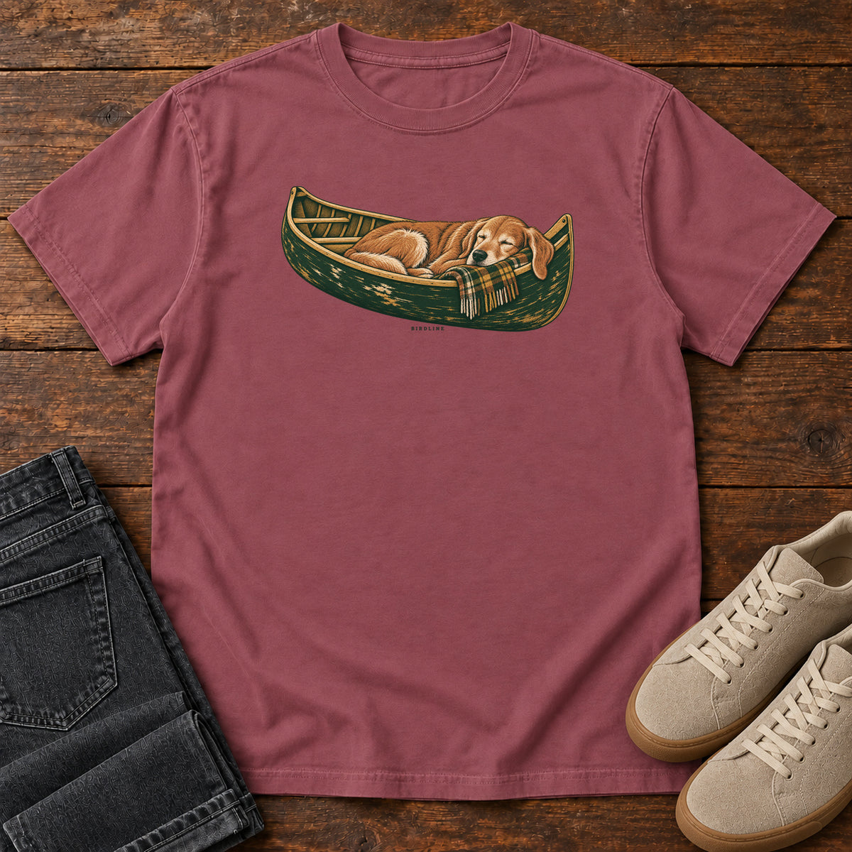Brick Retriever Canoe Birdline T-Shirt with a golden dog resting in a green canoe, front flat lay on wood.