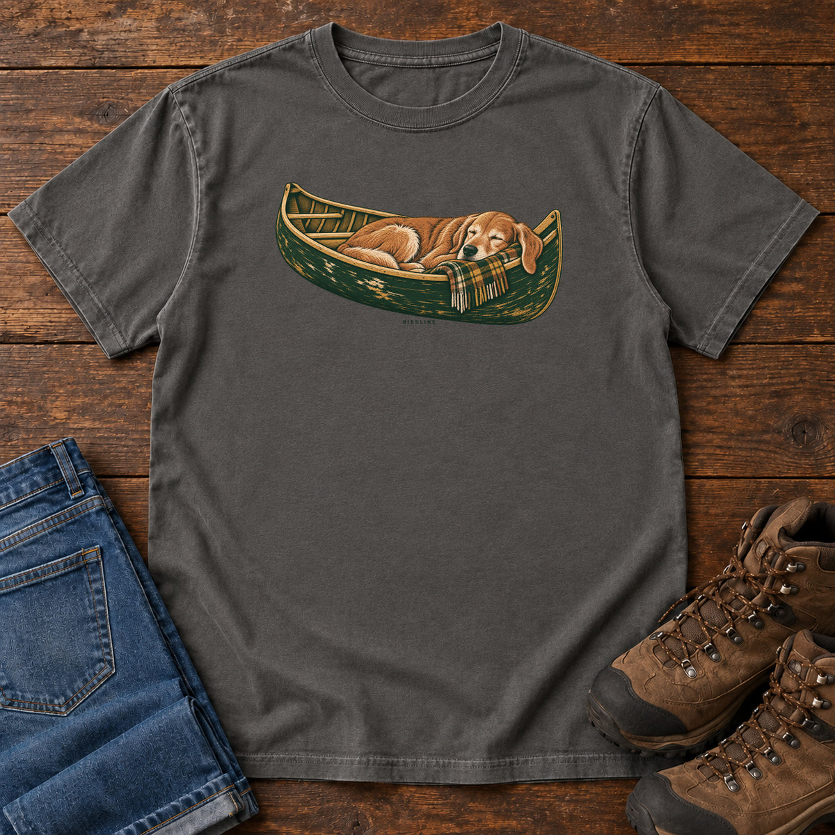 Pepper Retriever Canoe Birdline T-Shirt with a golden dog resting in a green canoe, front flat lay on wood.