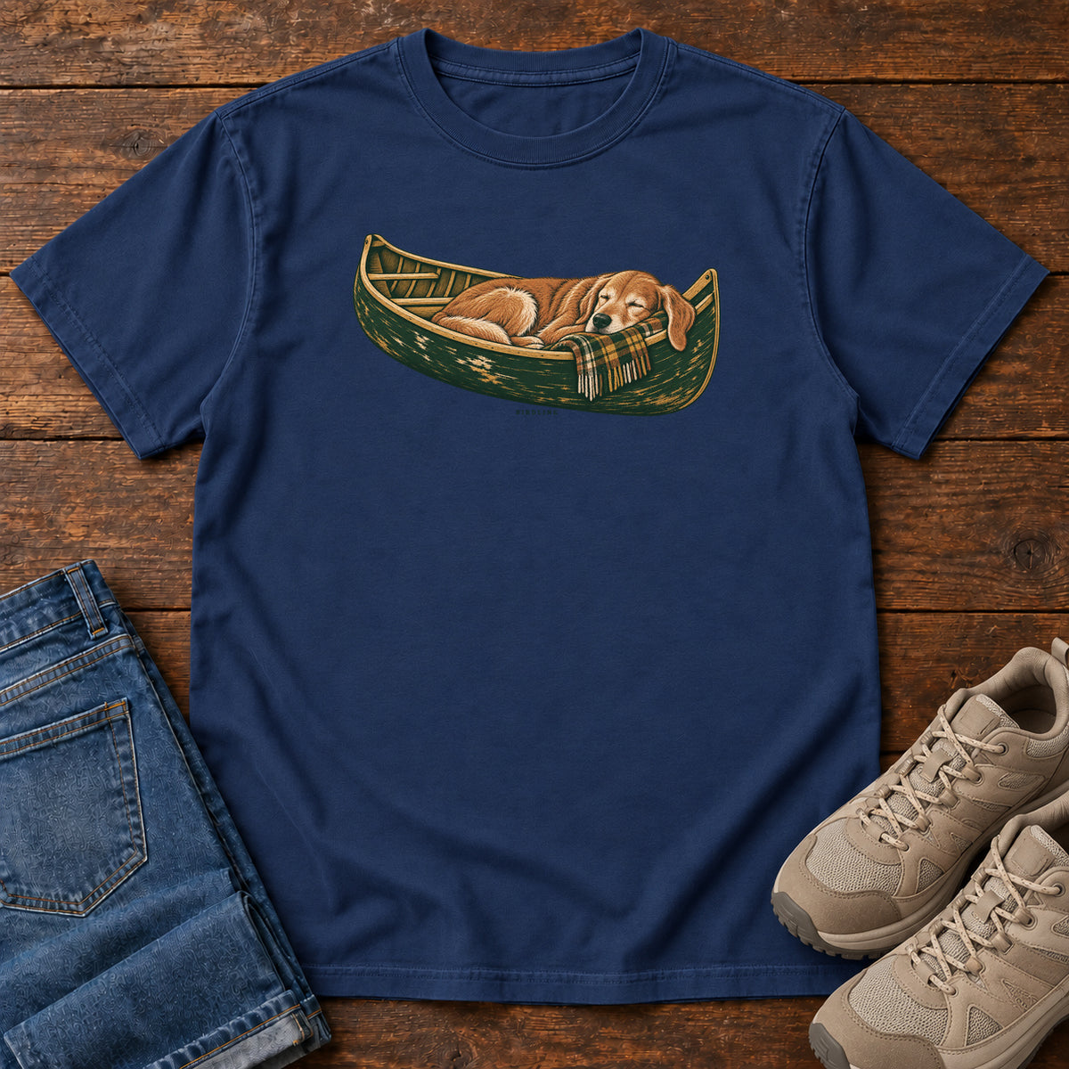 True Navy Retriever Canoe Birdline T-Shirt with a golden dog resting in a green canoe, front flat lay on wood.