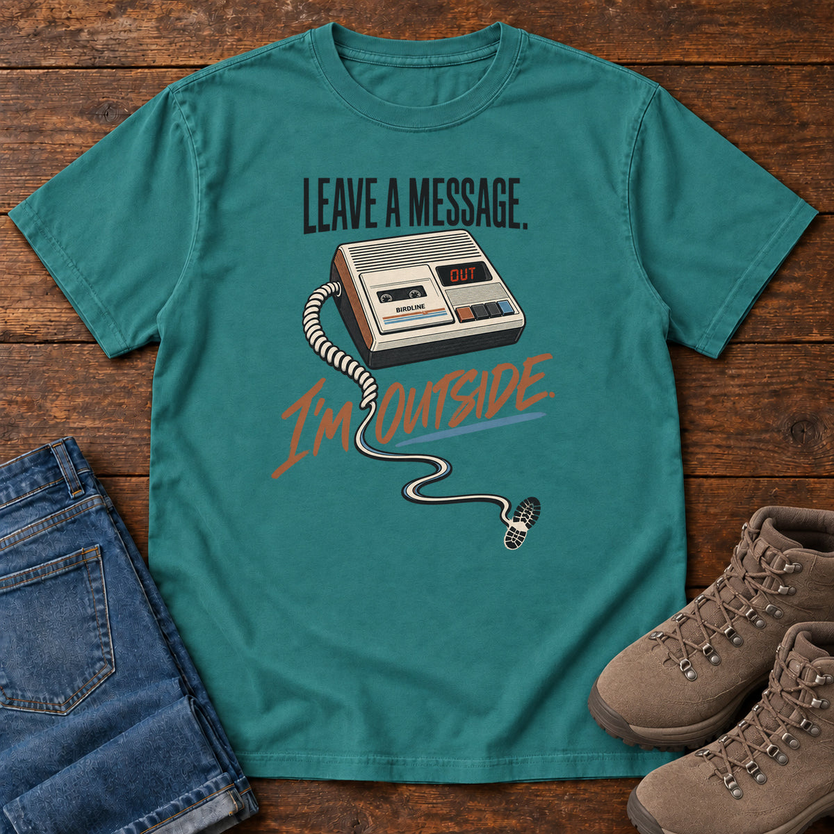Emerald Leave a Message I'm Outside T-Shirt with a retro answering machine, trailing cord and orange script, front flat lay on wood.