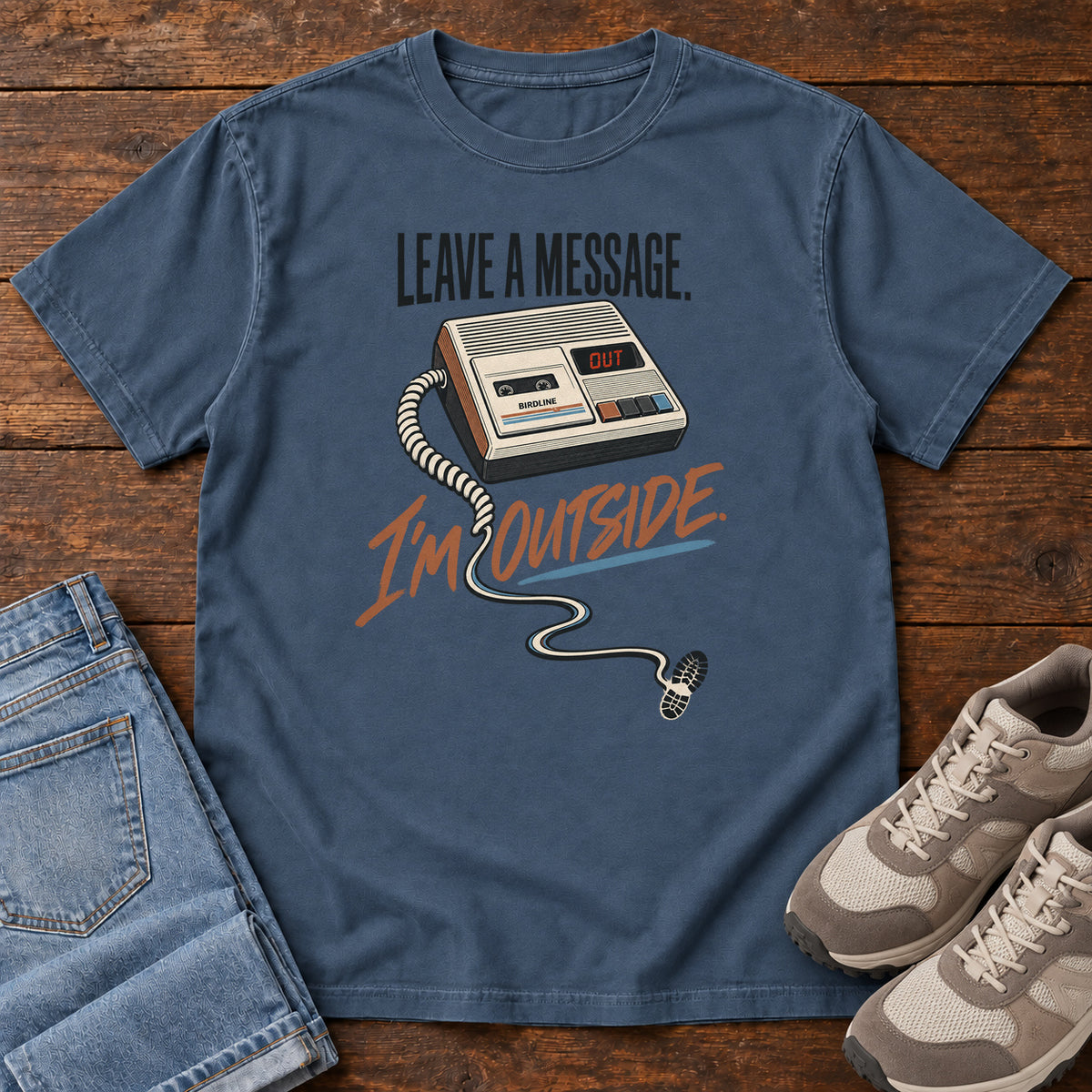 Midnight Leave a Message I'm Outside T-Shirt with a retro answering machine, trailing cord and orange script, front flat lay on wood.