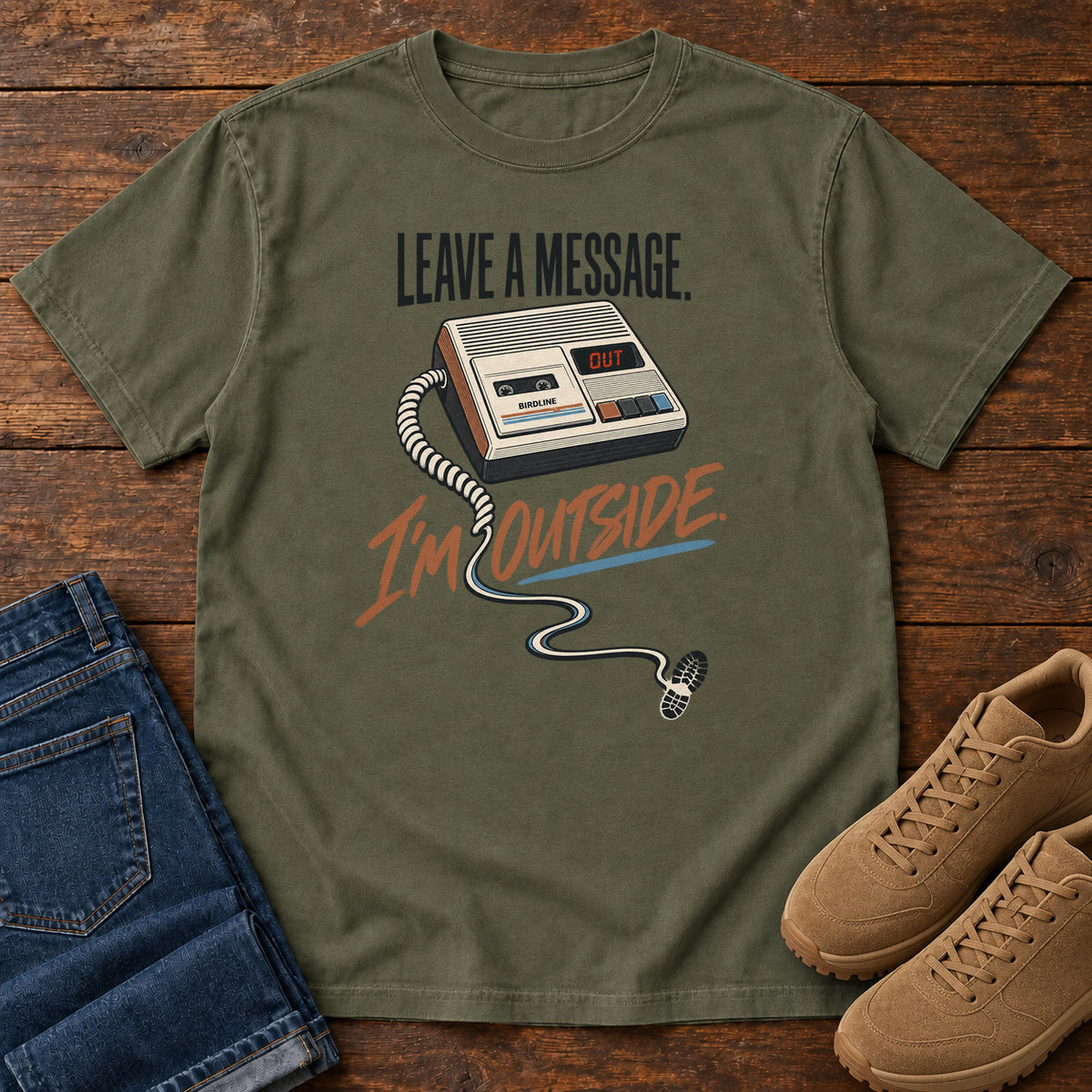 Sage Leave a Message I'm Outside T-Shirt with a retro answering machine, trailing cord and orange script, front flat lay on wood.