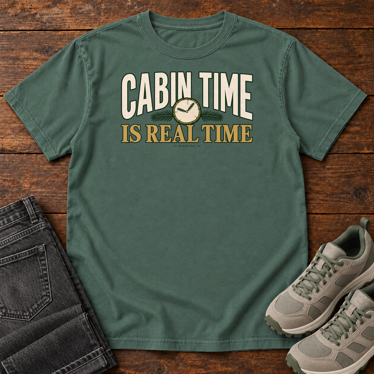 Blue Spruce Cabin Time Is Real Time T-Shirt with cream and gold lettering surrounding a small clock illustration, front flat lay on wood.