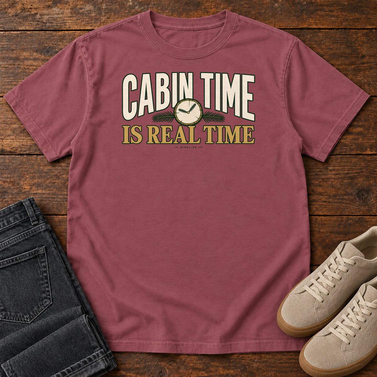 Brick Cabin Time Is Real Time T-Shirt with cream and gold lettering surrounding a small clock illustration, front flat lay on wood.
