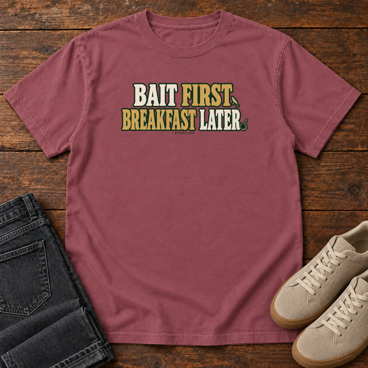 Brick Bait First Breakfast Later T-Shirt with cream and gold Bait First Breakfast Later lettering; front flat lay on wood.