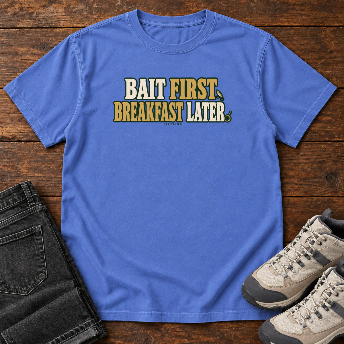 Mystic Blue Bait First Breakfast Later T-Shirt with cream and gold Bait First Breakfast Later lettering; front flat lay on wood.