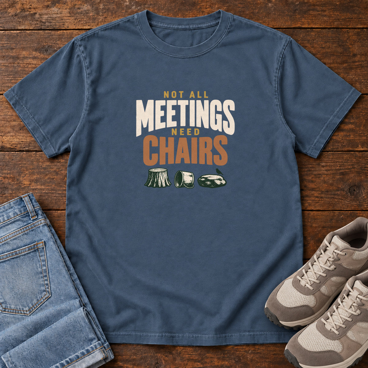 Midnight Not All Meetings Need Chairs T-Shirt with stacked cream-and-orange lettering above a stump, tipped mug and rock; front flat lay on wood.