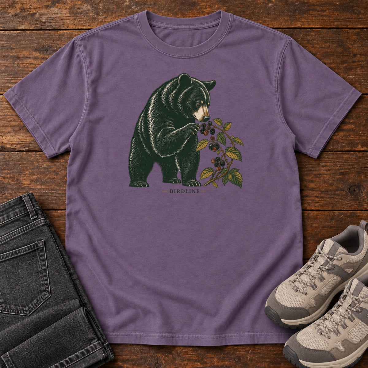 Grape Black Bear Berries Birdline T-Shirt with a dark bear holding a leafy berry branch, front flat lay on wood.