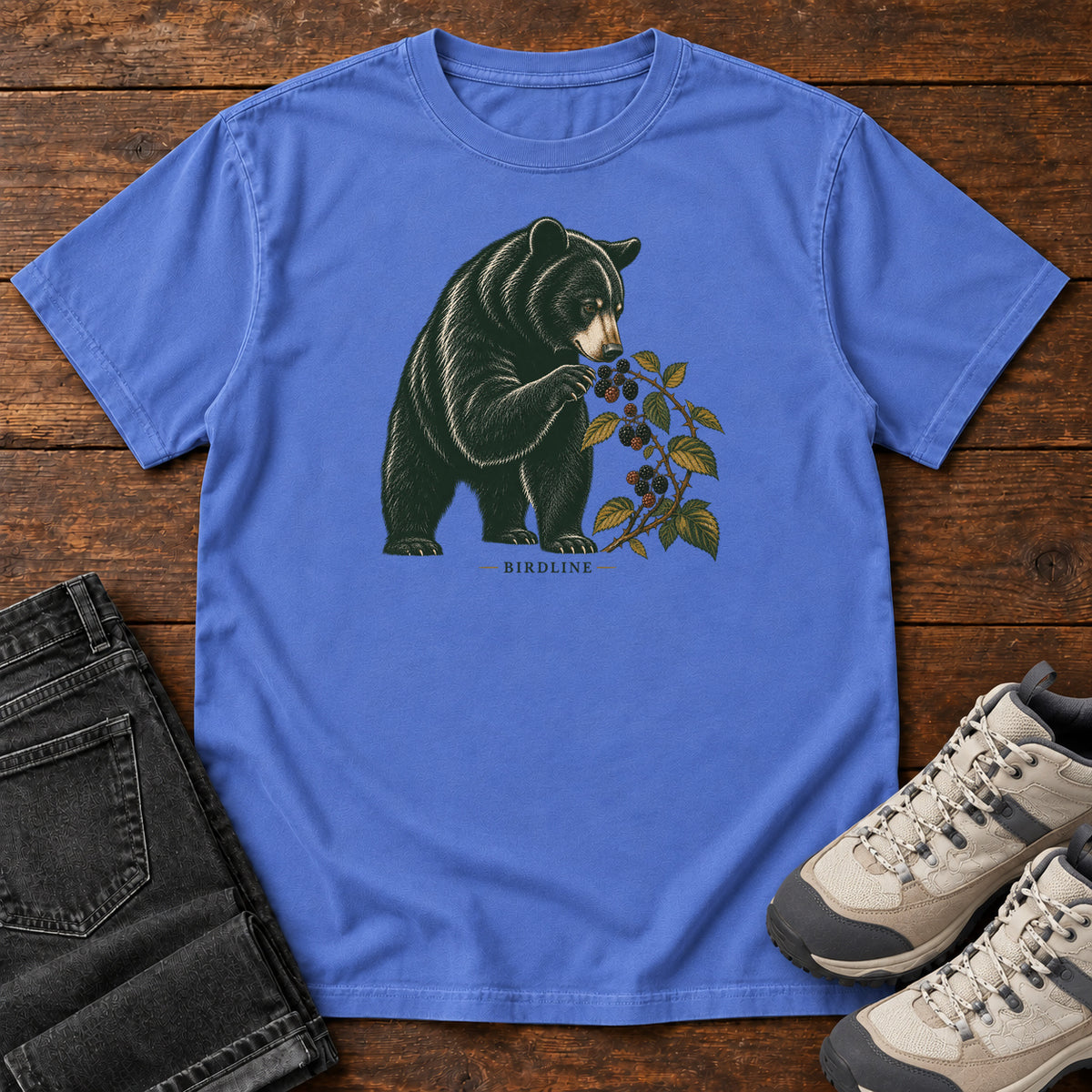Mystic Blue Black Bear Berries Birdline T-Shirt with a dark bear holding a leafy berry branch, front flat lay on wood.