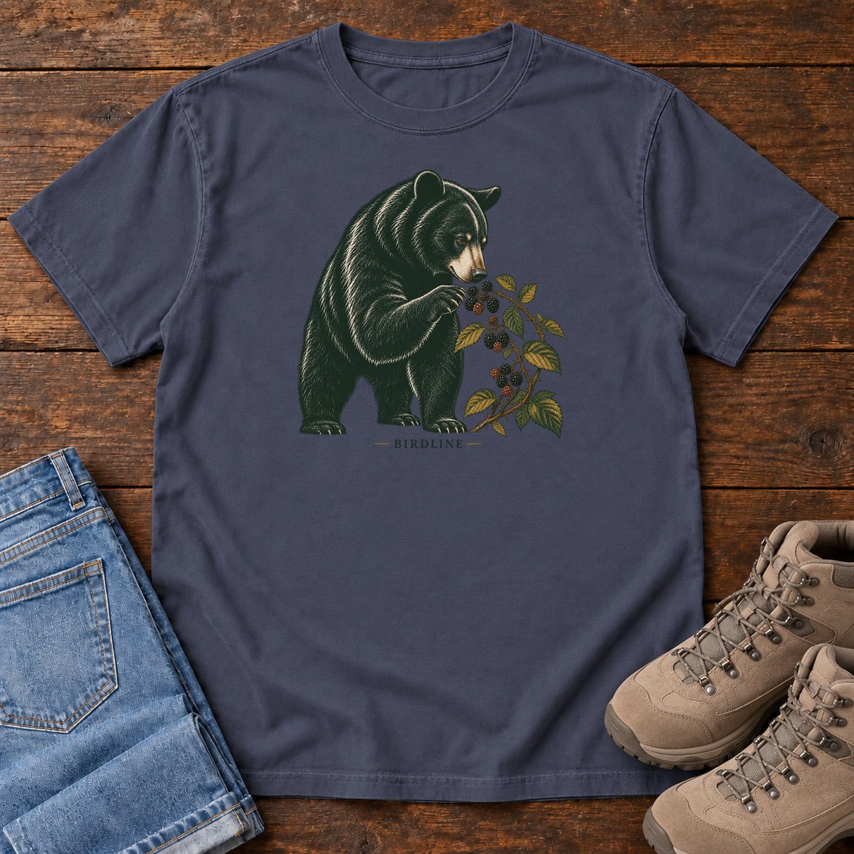 Navy Black Bear Berries Birdline T-Shirt with a dark bear holding a leafy berry branch, front flat lay on wood.