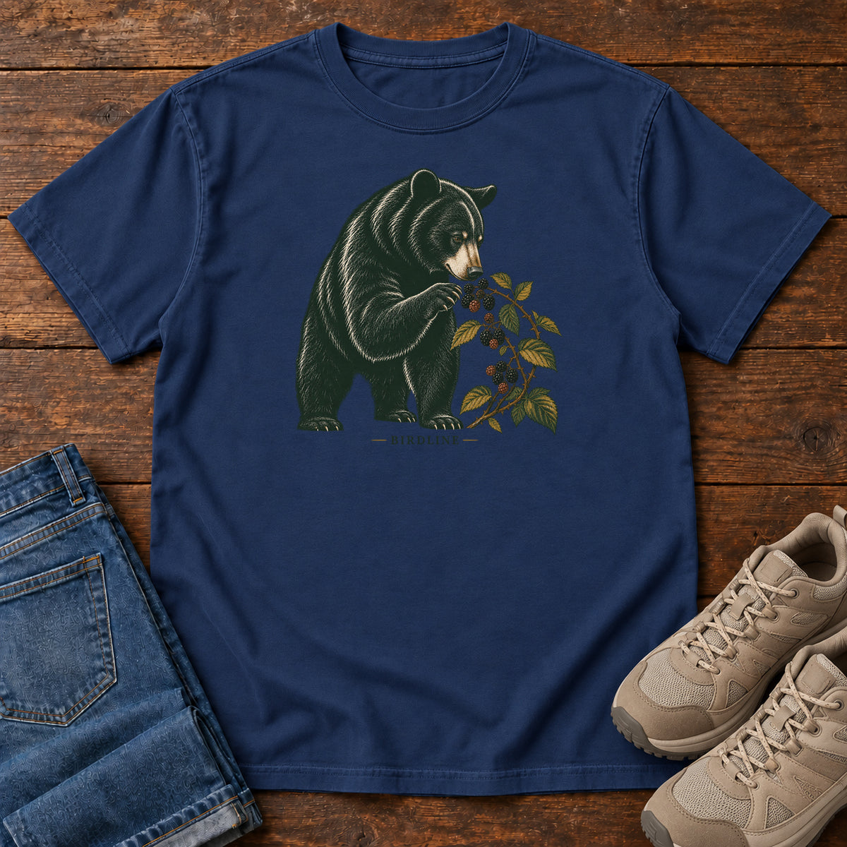True Navy Black Bear Berries Birdline T-Shirt with a dark bear holding a leafy berry branch, front flat lay on wood.