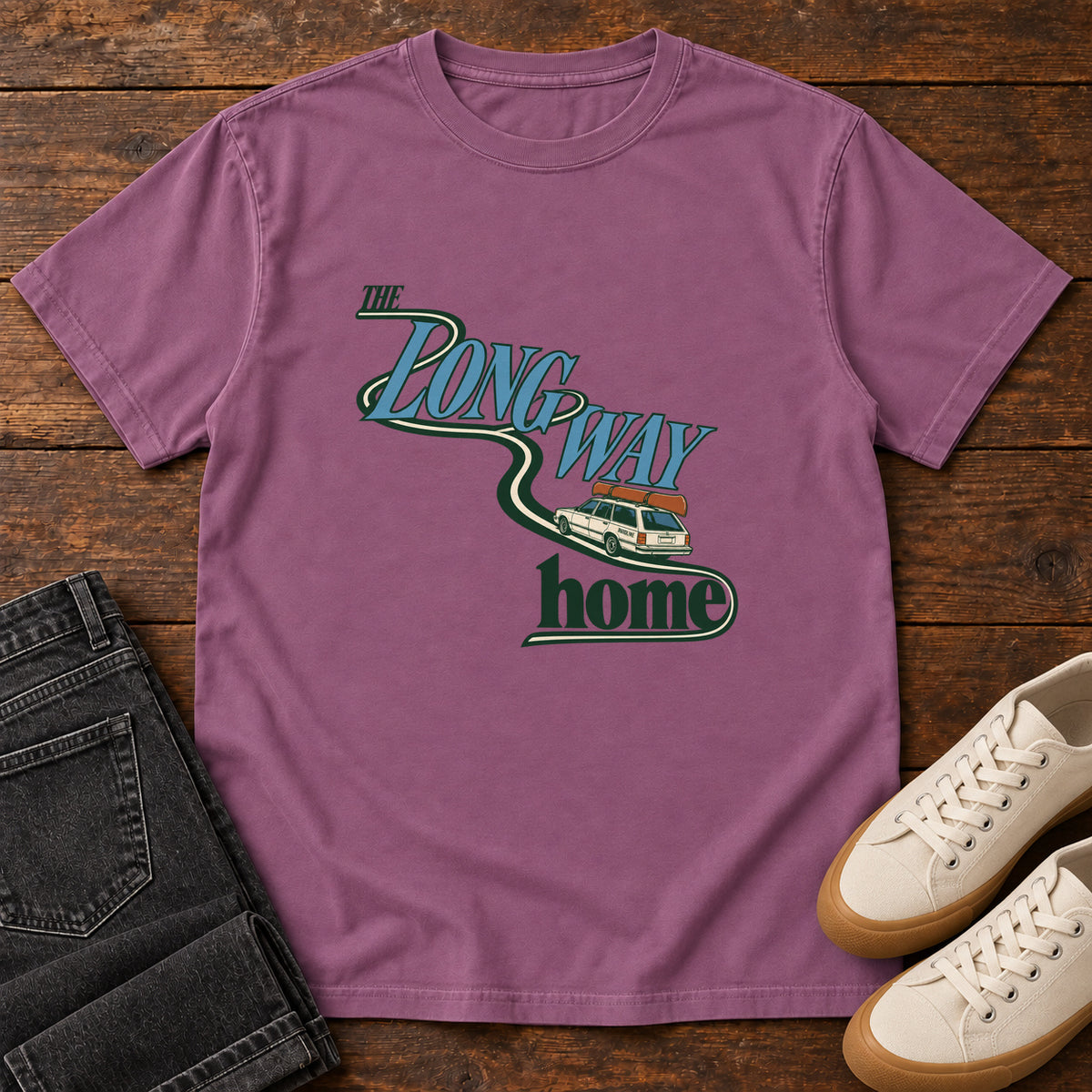 Berry The Long Way Home T-Shirt with a station wagon on a winding road woven through The Long Way Home lettering; front flat lay on wood.