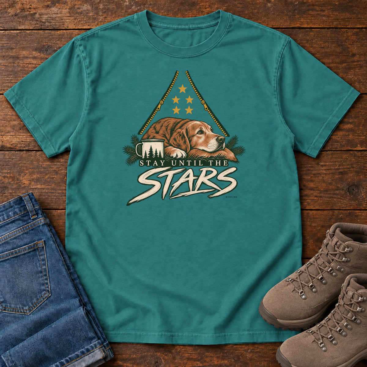 Emerald Stay Until the Stars T-Shirt with a resting brown dog beside a camp mug beneath gold stars and cream lettering, front flat lay on wood.