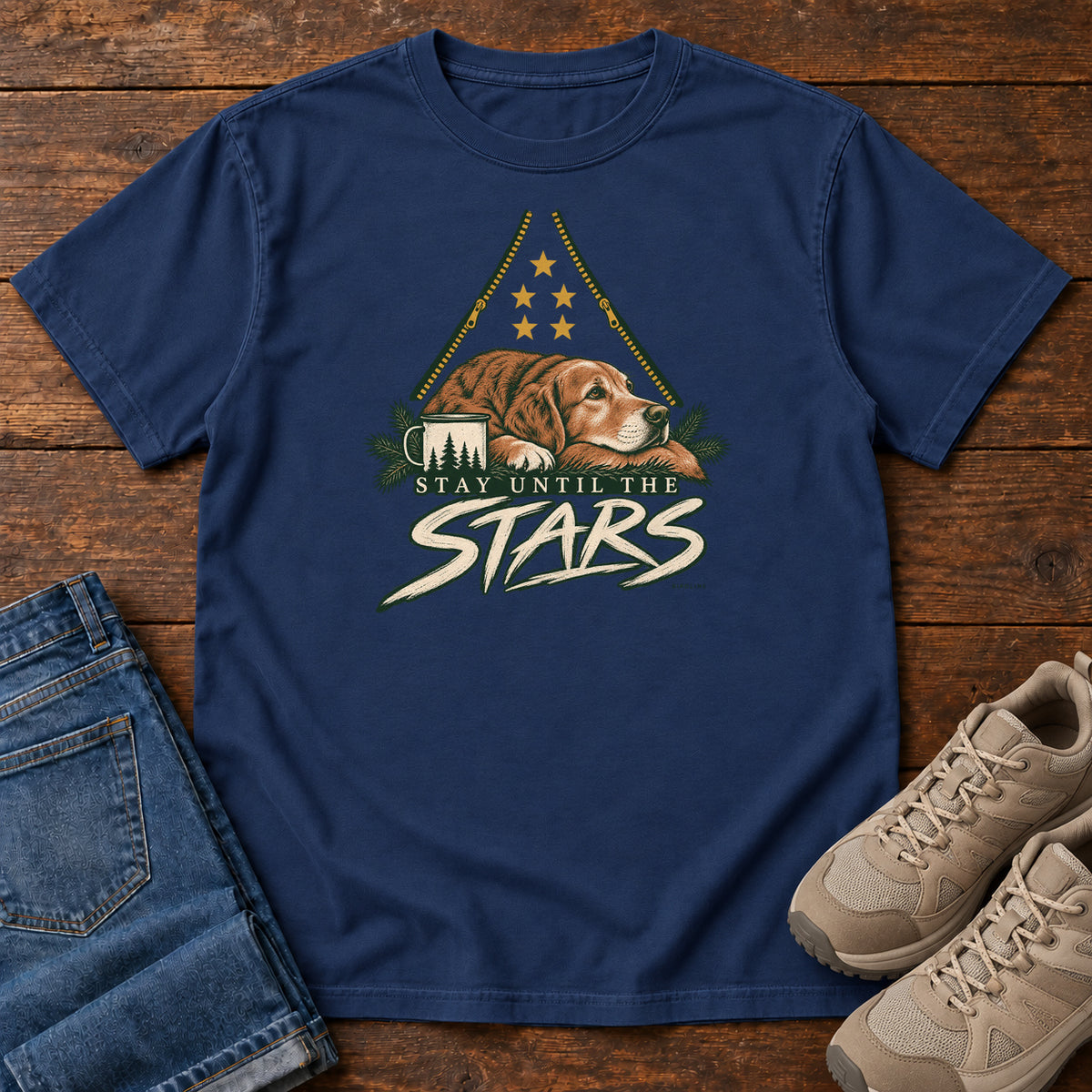 True Navy Stay Until the Stars T-Shirt with a resting brown dog beside a camp mug beneath gold stars and cream lettering, front flat lay on wood.