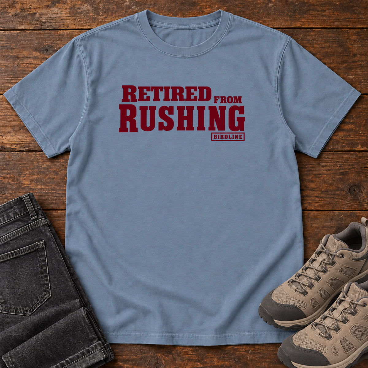 Blue Jean Retired From Rushing T-Shirt with burgundy Retired From Rushing lettering; front flat lay on wood.