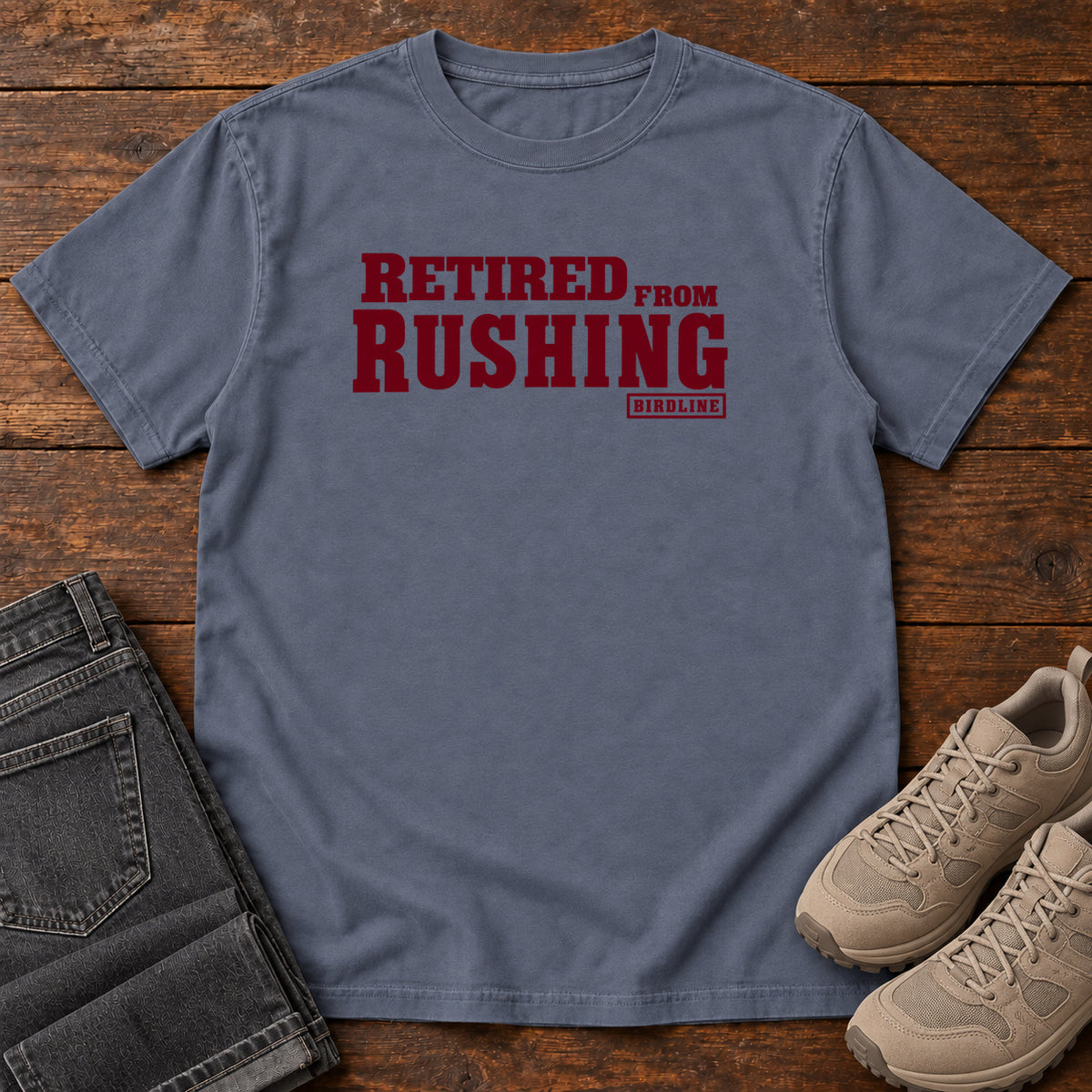 Denim Retired From Rushing T-Shirt with burgundy Retired From Rushing lettering; front flat lay on wood.