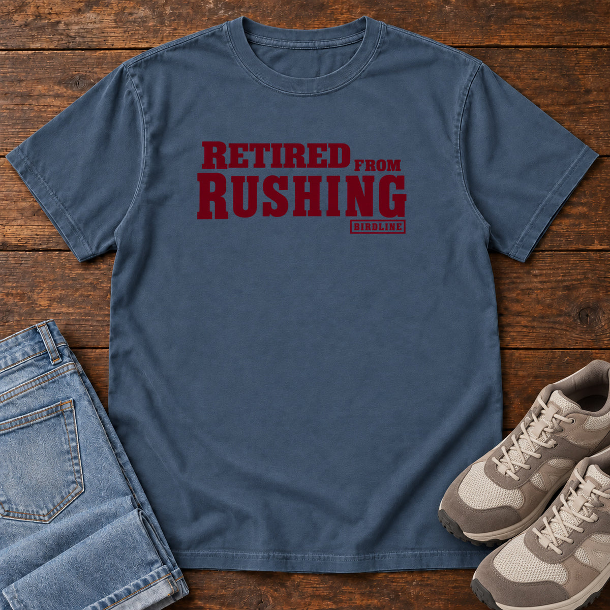 Midnight Retired From Rushing T-Shirt with burgundy Retired From Rushing lettering; front flat lay on wood.