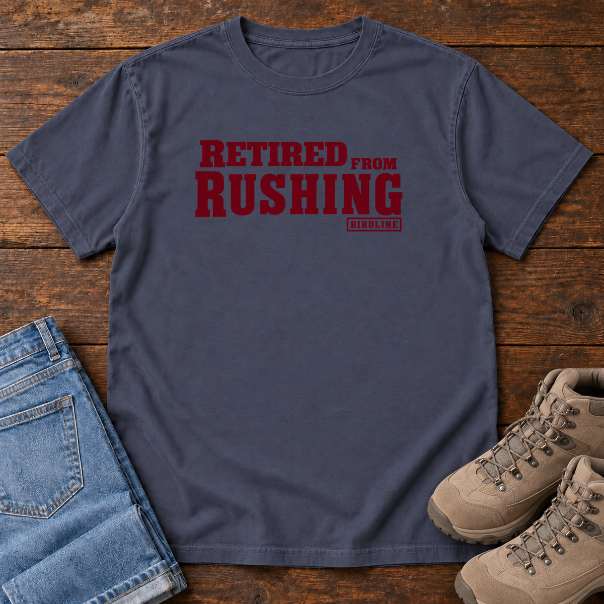 Navy Retired From Rushing T-Shirt with burgundy Retired From Rushing lettering; front flat lay on wood.