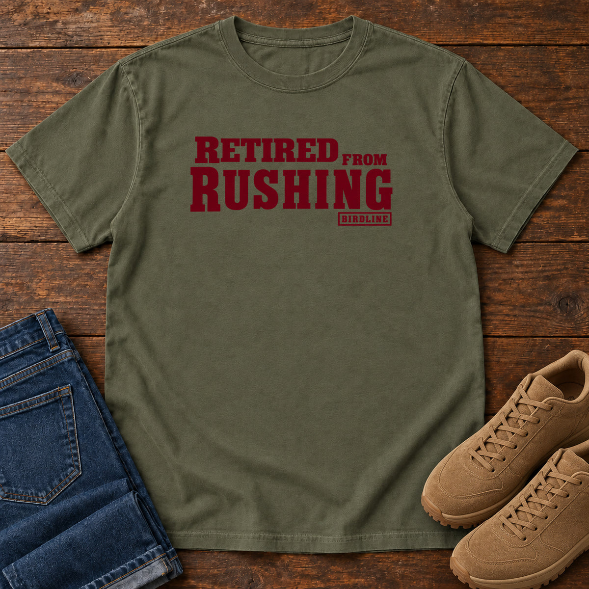 Sage Retired From Rushing T-Shirt with burgundy Retired From Rushing lettering; front flat lay on wood.