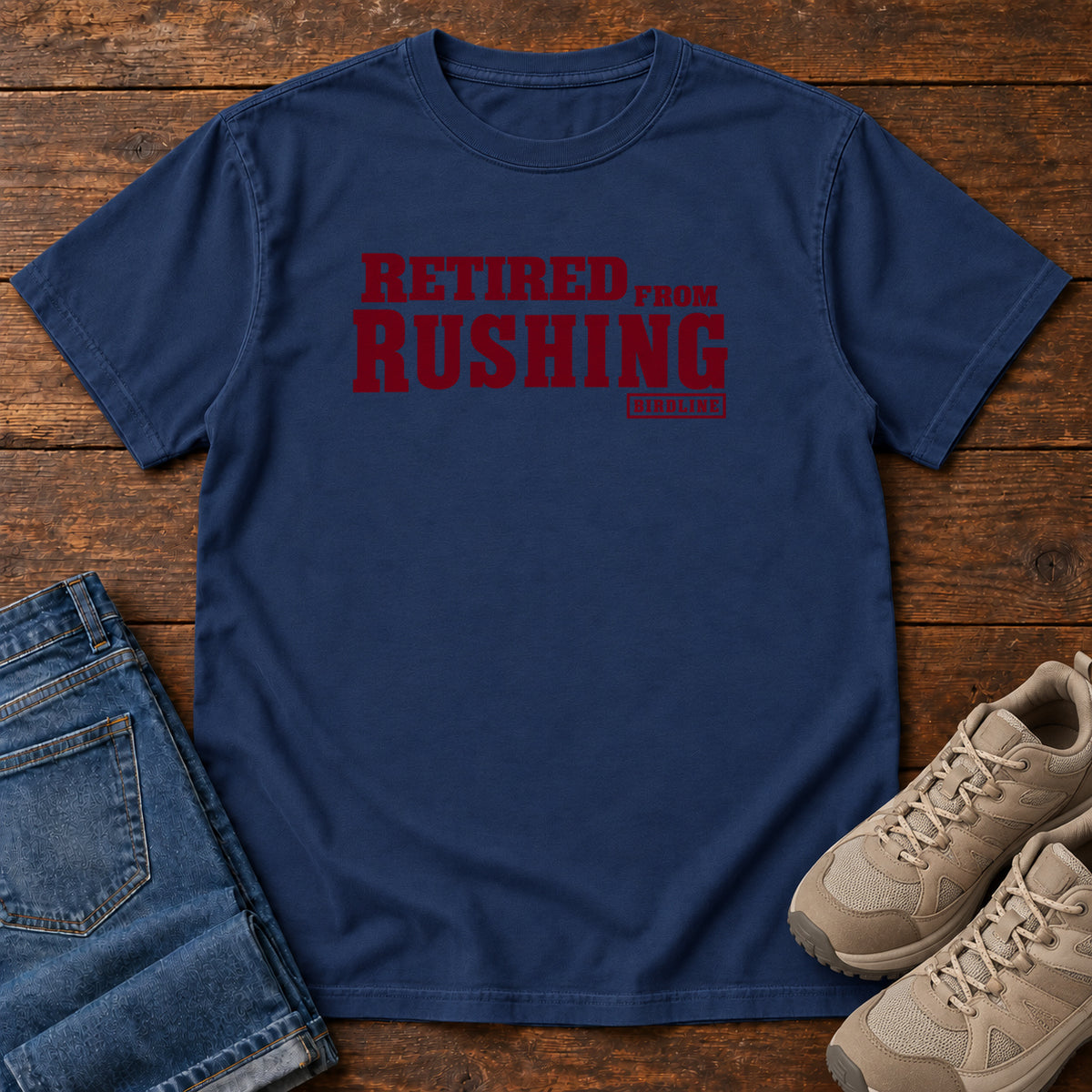 True Navy Retired From Rushing T-Shirt with burgundy Retired From Rushing lettering; front flat lay on wood.