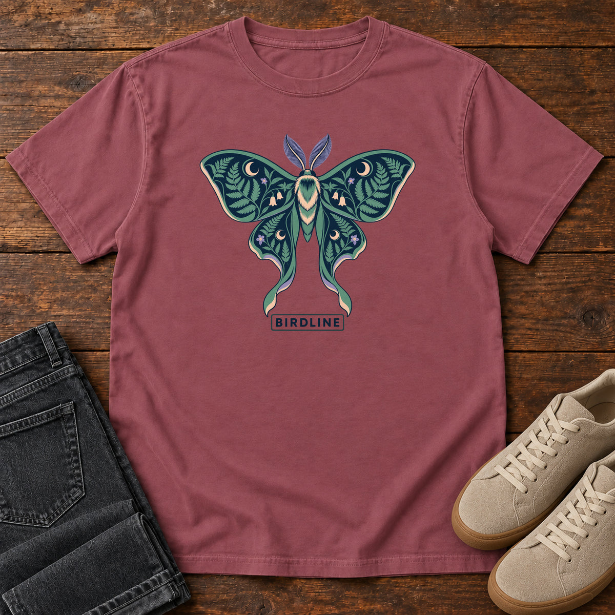 Botanical Moth T-Shirt in Brick, front laid flat on wood, featuring a teal moth with patterned wings, leaves and crescent moons.